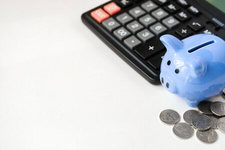 Blue piggy bank, calculator and coins on white background with copy space. The concept of budgeting.の写真素材
