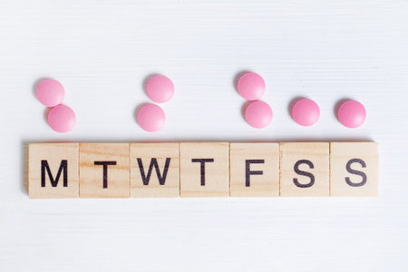 The concept of taking medication by day is the process of treatment. Pink tablets next to wooden frames with letters. Top view.の写真素材