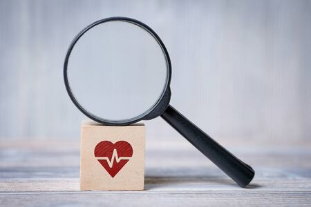 Close up of cube with heart with cardiogram icon and magnifier on wooden background. Concept of search medical information, health, cardiology.の写真素材