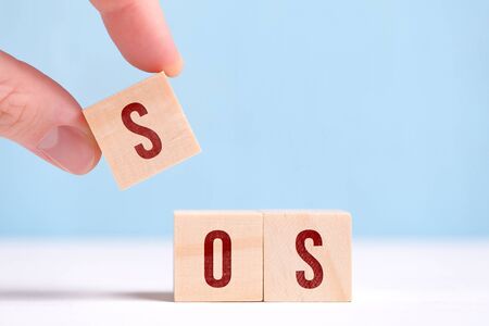 The concept of calling for the doctor's help - sos. Fingers hold a cube with a letter on a blue background. Close up.の写真素材