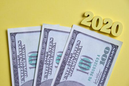 The concept of new investments in 2020. Dollars next to wooden figures on a yellow background. Top view. Close up.の写真素材