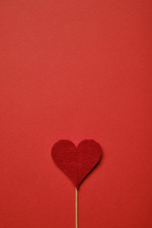 Red heart of fabric on a paper background. Top view. Copy space. Close up.