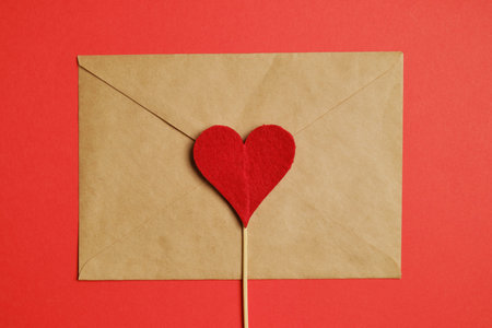 Red heart on a stick with a craft envelope on a paper background. Top view. Close up.