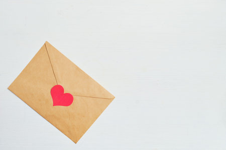 Red heart with a craft envelope on a white wooden background. Top view. Copy space. Close up.