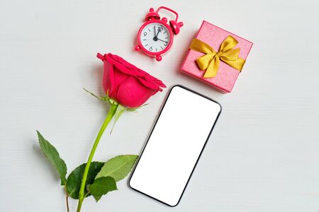 Smartphone copy space with a one red roses, watches, gift box on a white wooden background. Top view.の写真素材