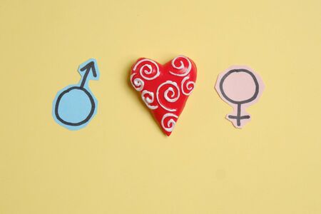 Signs of difference between a man and a woman next to the heart on a yellow background. The concept of love and Valentine's Day - 14 feral. Close up.の写真素材