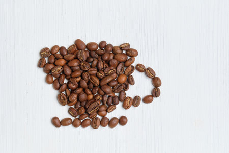 Abstract cup made of roasted coffee beans on a white wooden background. Top view.