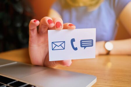 The girl holds a white card with abstract icons for communication - mail, phone, message. Close up.の写真素材
