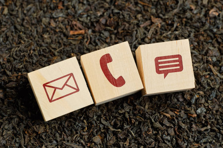 Abstract contact icons - envelope, phone, message - on wooden cubes and dry tea. Close up.