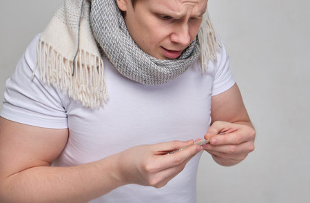A man in a white T-shirt with a scarf looks at the thermometer in surprise. The concept of lowered...