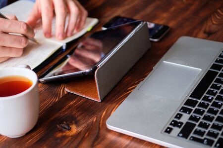 A man in a shirt makes notes in a diary and works on a laptop and tablet. Analytics activity concept. Close up.の写真素材