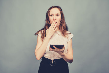A brunette girl in casual clothes with a tablet looks at the camera and makes a very surprised face. Toned. Close up.の写真素材