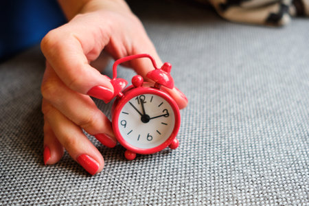 The girl holds an analog clock in red. Limited time concept for action selection. Close up.の写真素材