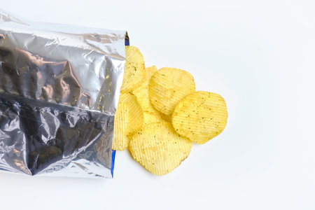 Chips are falling out of foil packaging on a white background. Close up.