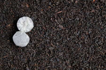Round bundles of tea on a background of dry scattered black tea. Copy space. Top view. Close up.の写真素材