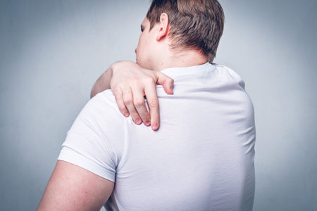 A man massages his neck, scratches his back. Severe itching. Allergy reaction. Toned. Close up.