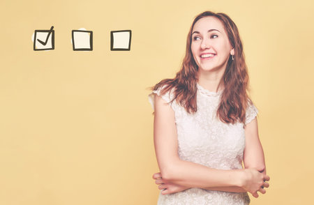 A girl in summer clothes stands on a yellow background and smiles with clasped hands and looks at...