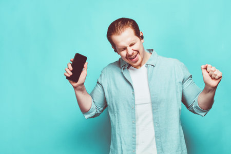 A man in casual clothes on a blue background holds a smartphone in his hands and dances in wireless...