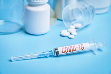 Syringe with the inscription COVID-19 on the background of medical equipment. blue background. Close up.の写真素材