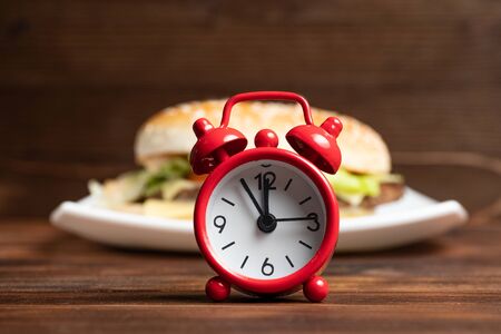 Red clock and burger on a white plate and wooden background. Close up.の写真素材