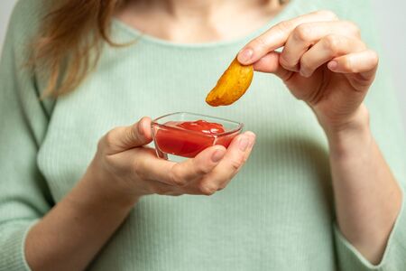 Girl holds a plate and eats a rustic potato with ketchup in paper. Close up.の写真素材