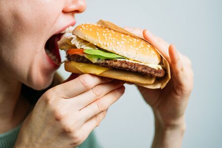 The girl holds a hamburger with her hands and bites it. Close up.の写真素材