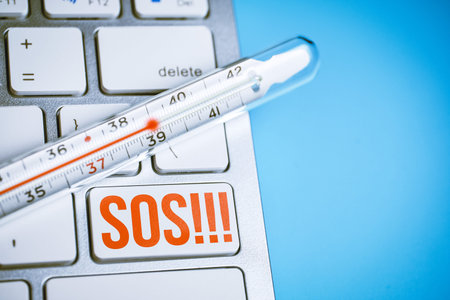 Thermometer on a keyboard with a button sos on a blue background. Close up.