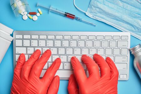 A doctor in red gloves works at a computer on a blue background near medical equipment. Top view.の写真素材