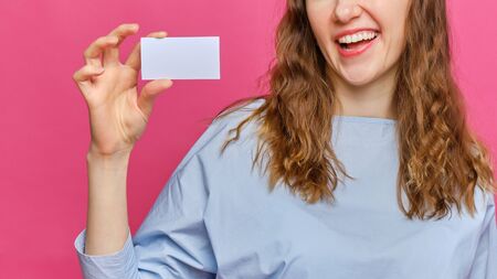 Stylish caucasian girl in a pale blue t-shirt hands holding a white card on a pink background. Copy space. Close up.の写真素材