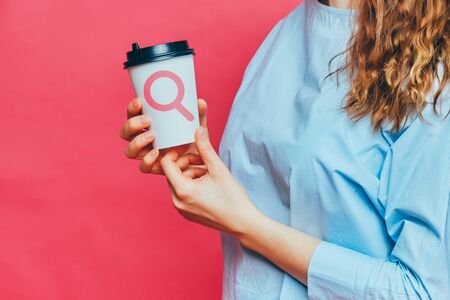 Stylish caucasian girl in a pale blue t-shirt on a pink background. The concept of finding coffee or goods for manufacturing. Close up.の写真素材