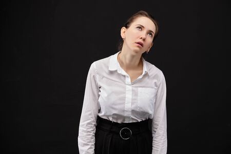 A girl in a white shirt on a black background is a very tired workaholic. Close up.の写真素材