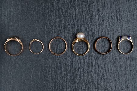 A set of different golden rings on a black stone board. Top view. Close up.の写真素材