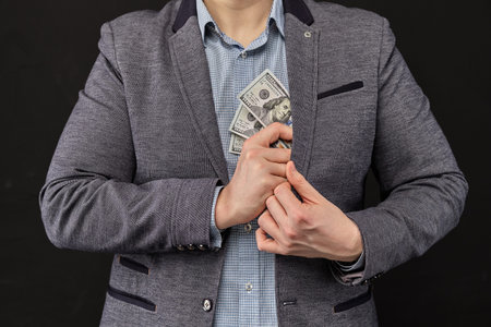 A man in a jacket removes us dollars in a jacket on a black background. Close up.