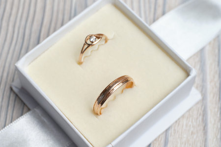 Gold wedding rings in a white box on a wooden background. Close up.