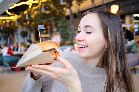 The girl holds a burger in her hands and looks at him. Close up.の写真素材