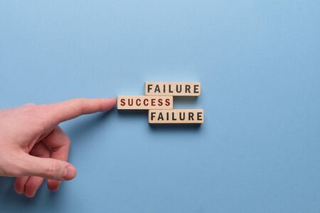 Failure and success concept - hand holds wooden block with the inscription on a blue background. Close up.の写真素材