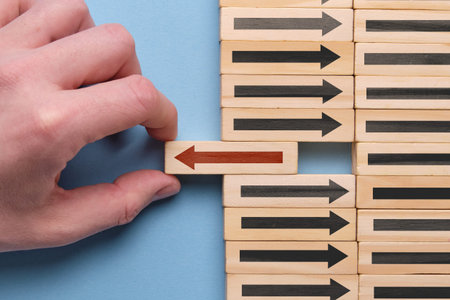 Alternative business development concept - hand holds wooden cube with red arrow on blue background. Close up.の写真素材