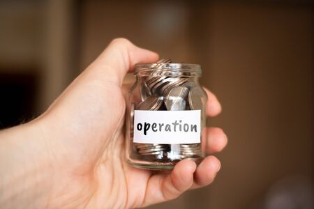 The concept of savings for the operation - Glass jar with coins and the inscription. Close up.の写真素材