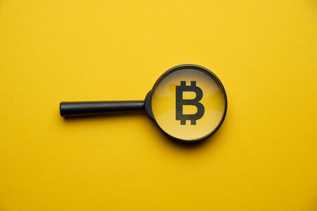 Bitcoin cryptocurrency search concept with magnifying glass on a yellow background. Close up.の写真素材
