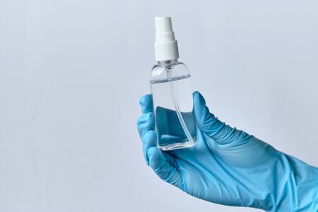 A hand in blue medical gloves holds a sanitizer antiseptic against a white background - concept of protection against coronavirus COVID-19. Close up.の写真素材