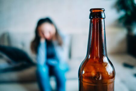 Bottle of alcohol with a drunk woman on the background as a concept of problems in the house. Close up.の写真素材