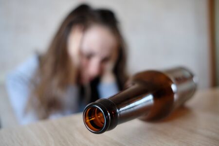 A bottle of alcohol on the table and the girl on the background clutched her head. Close up.の写真素材