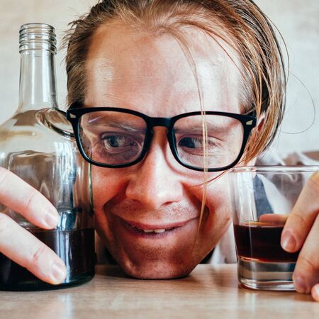 Portrait of a man with glasses between a bottle and a glass of whiskey. Close up.の写真素材