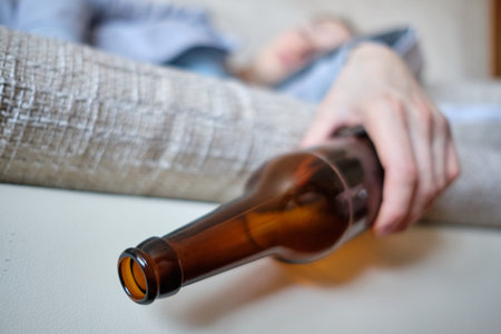 The girl sleeps on the couch and holds in his hands a bottle of alcohol. Close up.