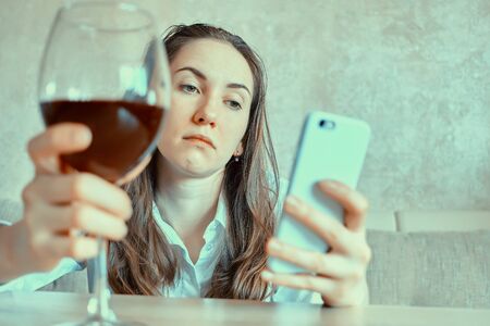 Girl holds a glass of wine and writes a message on a smartphoneの写真素材
