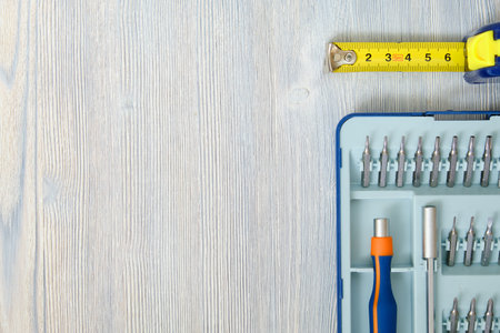 Screwdriver with interchangeable nozzles and tape measure with meter on a wooden gray background...