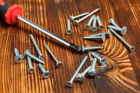 Screwdriver next to different screws on a wooden backgroundの写真素材