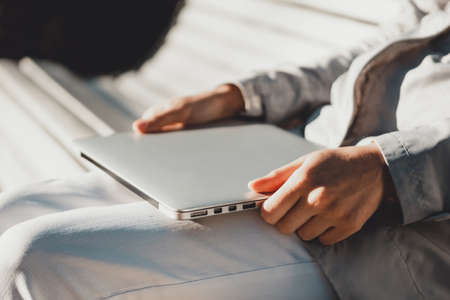 Caucasian girl sitting in a park on a bench with a closed laptop.の写真素材