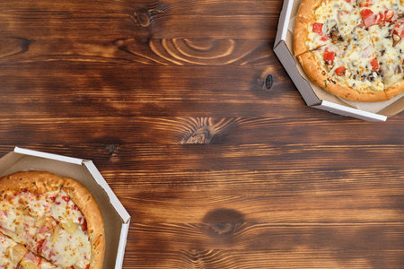 Hawaiian pizza and carbonara in cardboard packaging on a wooden background with top view and copy...