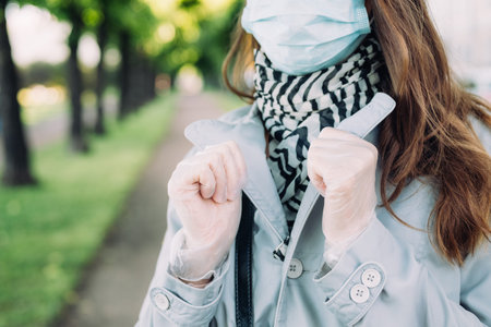Caucasian girl in a medical mask and a gray coat walks in the park.